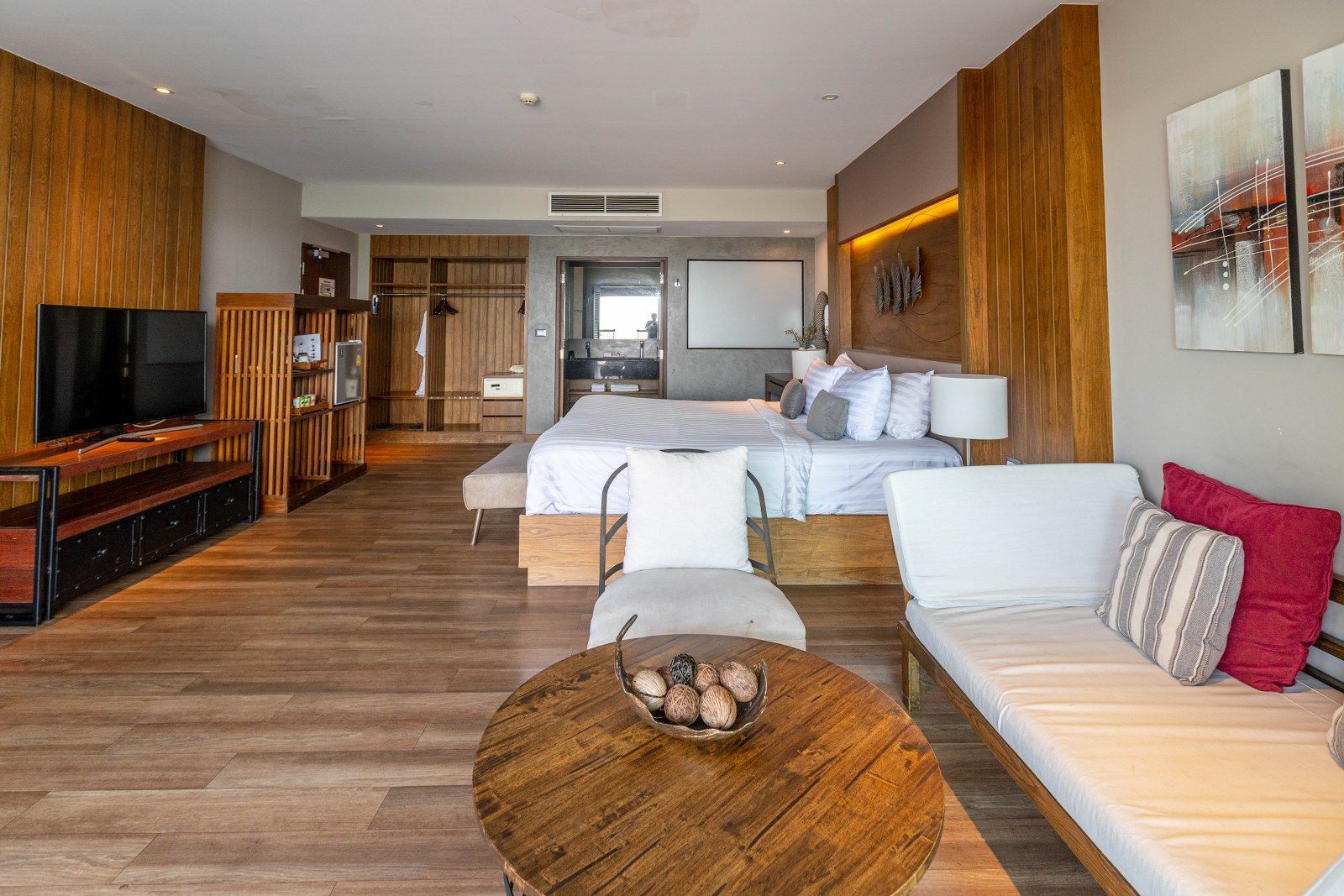 Hotel room with a bed, TV, sofa, and round wooden table. Wooden paneling and hardwood floors.