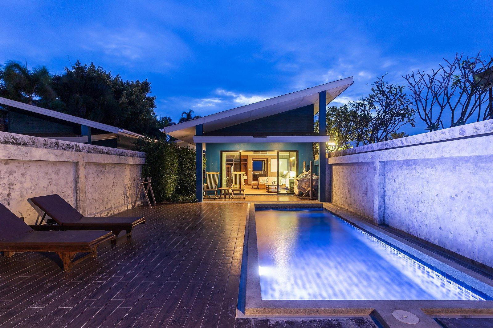 Poolside villa at dusk, with pool, lounge chairs, and teal exterior walls.