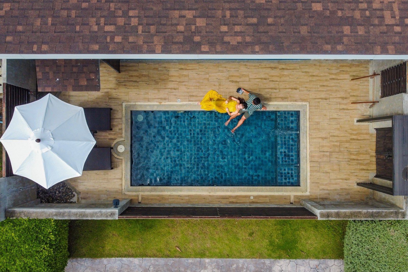 Overhead view of a pool with two people in it, next to a white umbrella.