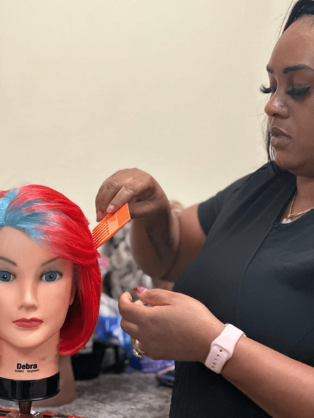 A woman is combing a mannequin head with red and blue hair.