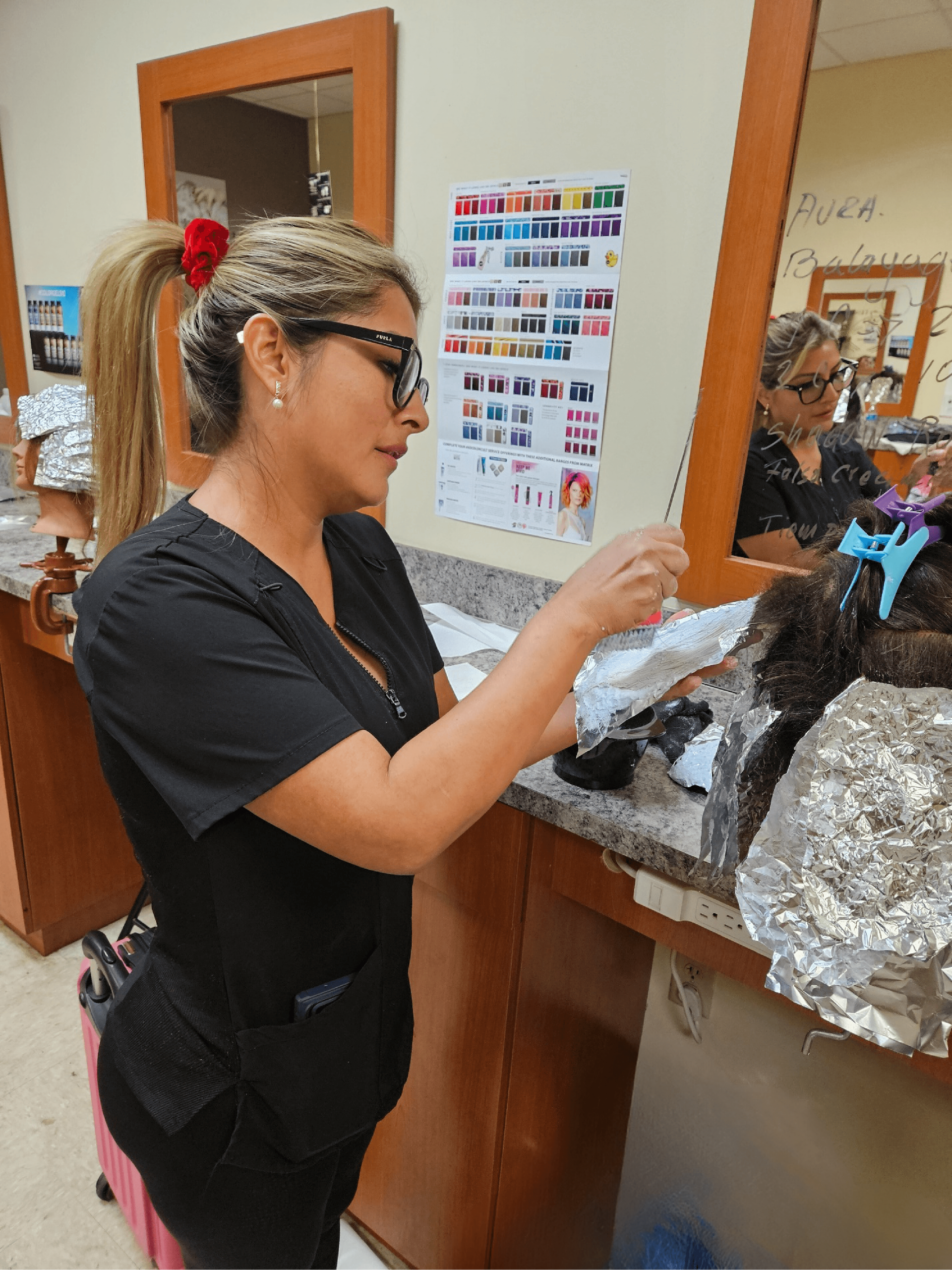 A woman in a black scrub top is working on her hair in front of a mirror.