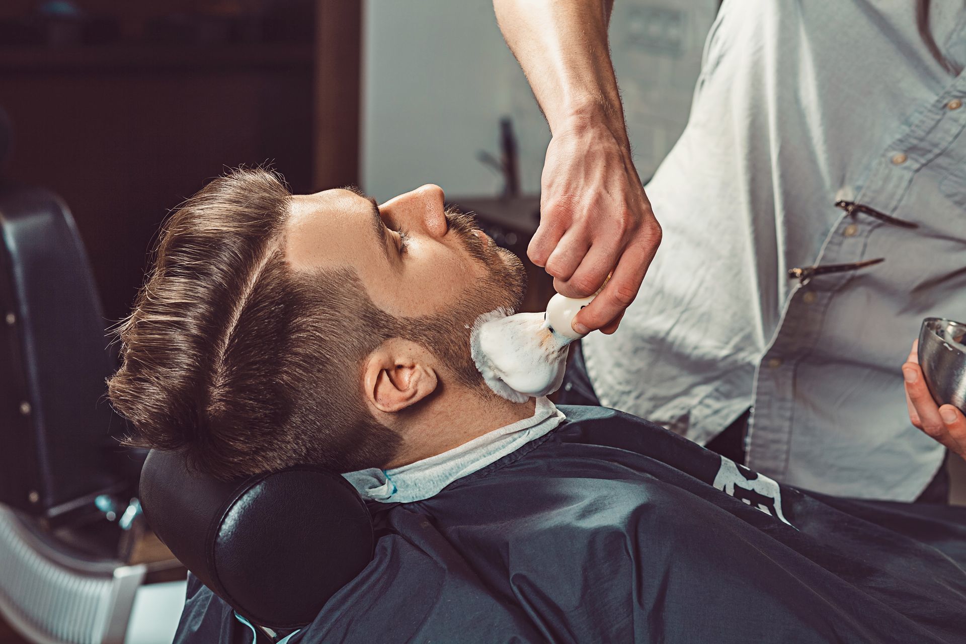 A man is getting his beard shaved by a barber in a barber shop.
