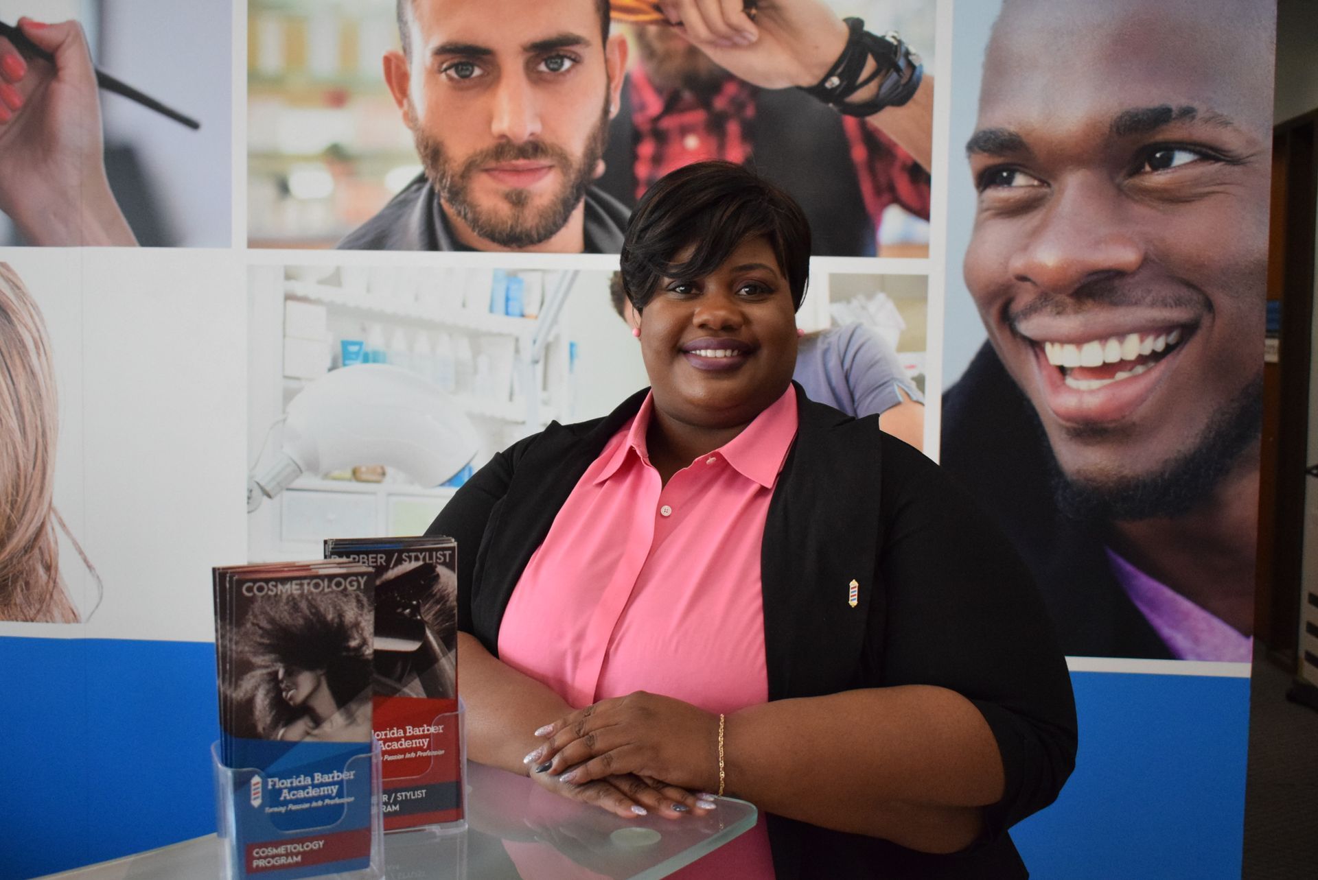 A woman in a pink shirt is standing in front of a wall with pictures of people 's faces.