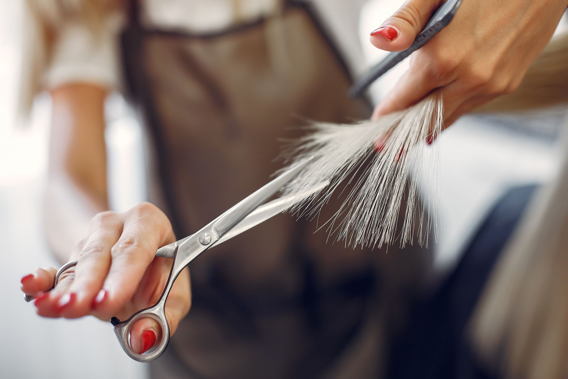 A man is getting his hair cut by a barber with scissors and a comb.