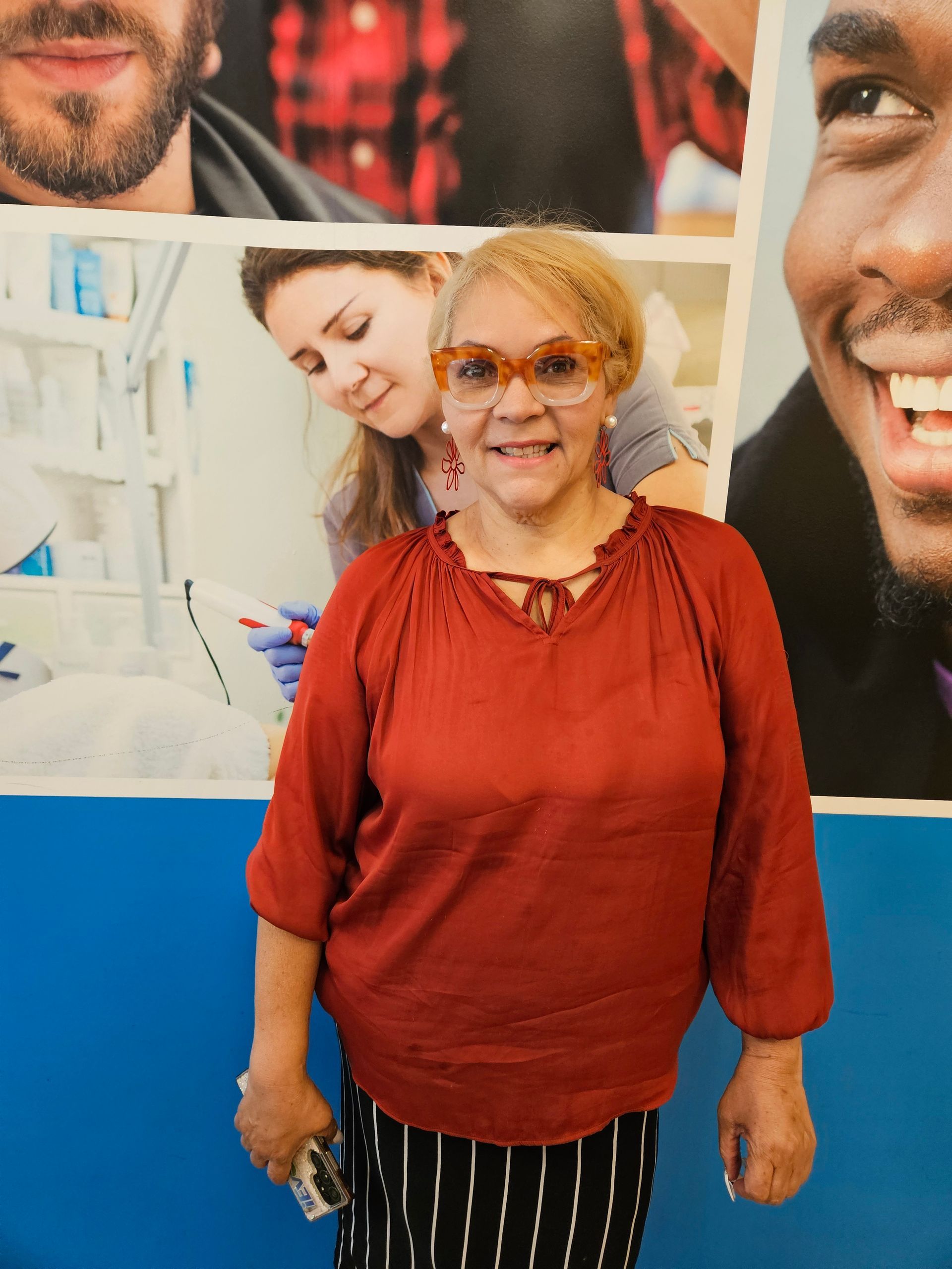 A woman wearing glasses and a red shirt is standing in front of a blue wall.