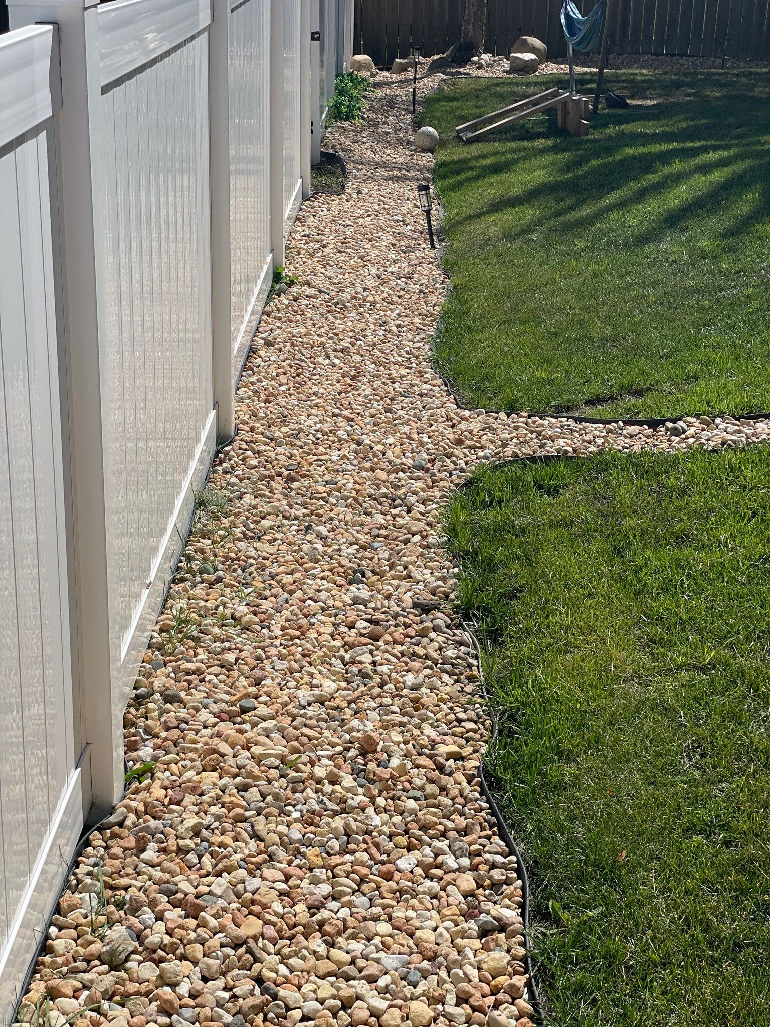 A gravel path leading to a white fence in a backyard.