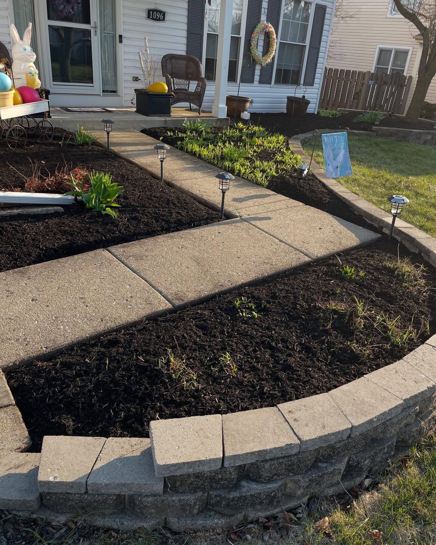 A concrete walkway leading to a house with a garden in front of it.
