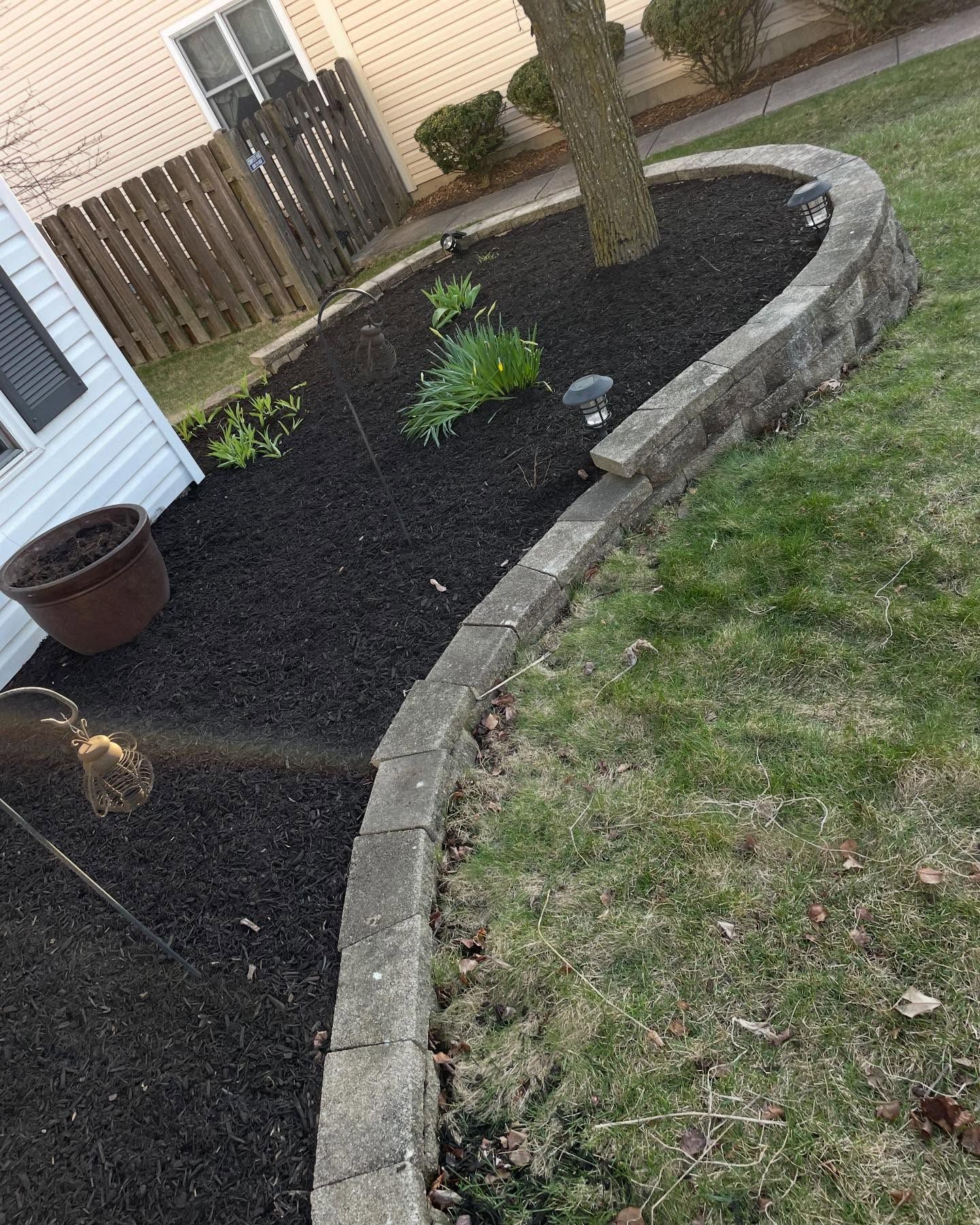 A lawn with a brick border and black mulch in front of a house.