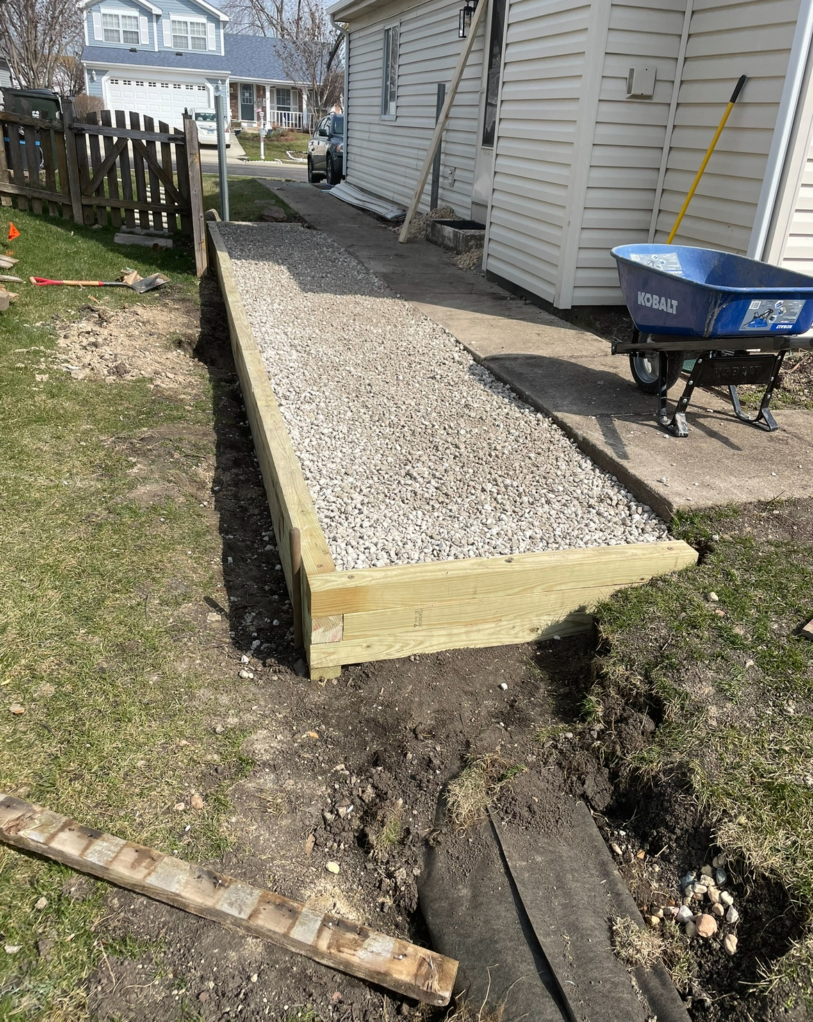 A wheelbarrow is sitting next to a wooden walkway in front of a house.