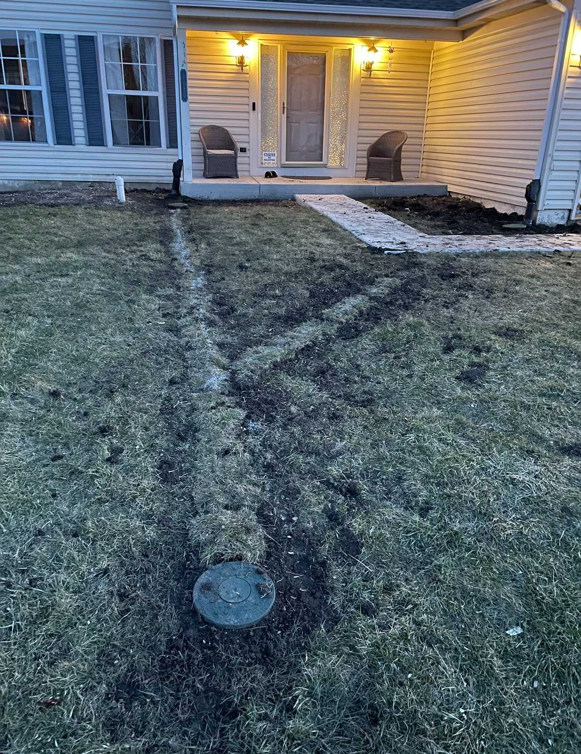 A house with a walkway leading to the front door and a drain in the yard.