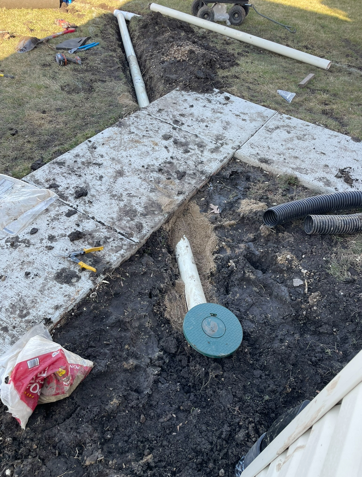 A drain pipe is being installed in the dirt next to a sidewalk.
