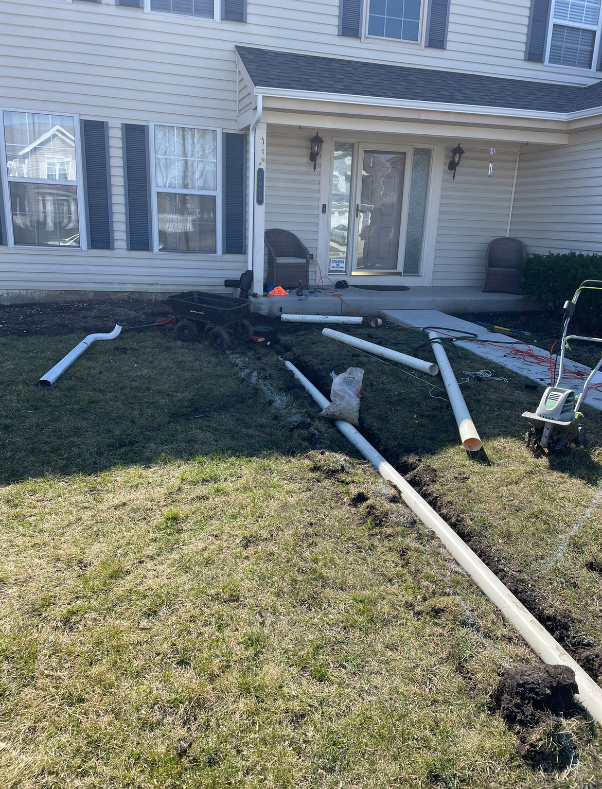 A bunch of pipes are laying in the grass in front of a house.