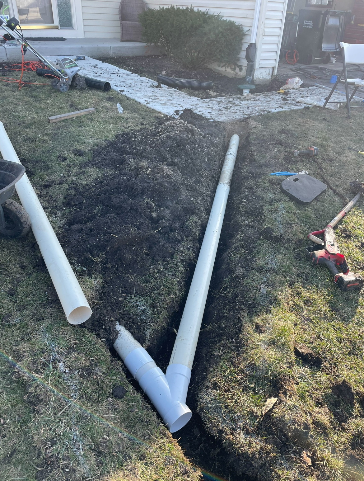 Two white pipes are laying in the dirt in front of a house.