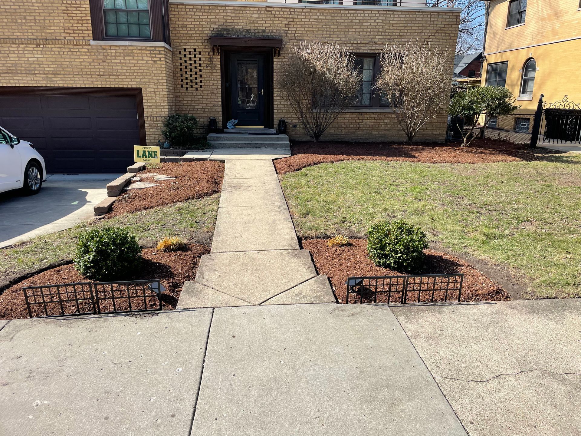 A white car is parked in front of a brick house.
