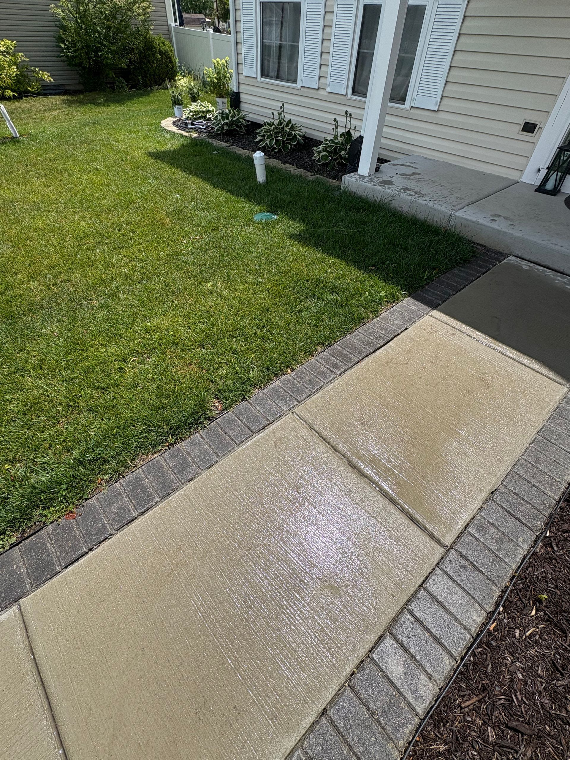 A concrete walkway leading to a house with a lush green lawn.