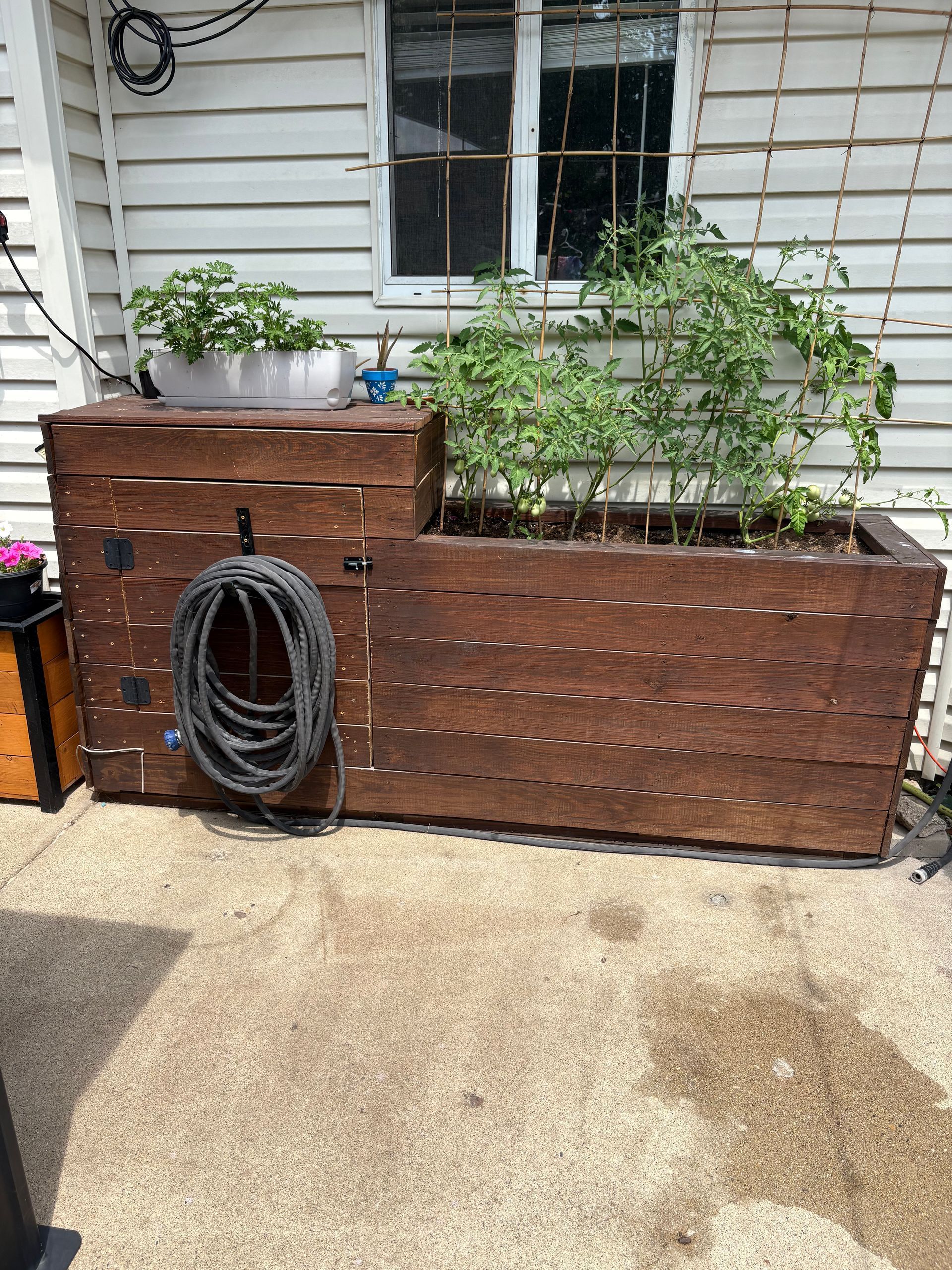 A wooden planter with a hose attached to it is sitting on a patio in front of a house.