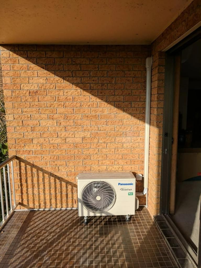 An Air Conditioner Is Sitting on A Balcony Next to A Brick Wall — Gleeson's Air Conditioning in Port Macquarie, NSW