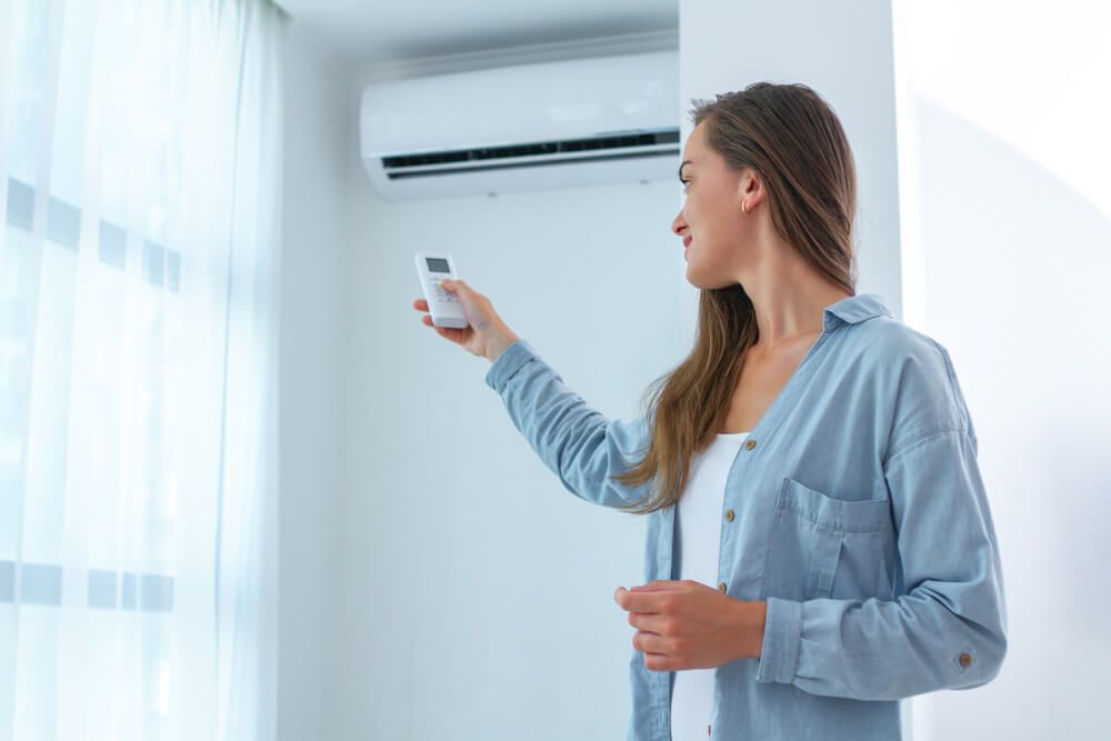 A woman is adjusting the temperature of her air conditioner with a remote control — Gleeson's Air Conditioning in Bonny Hills, NSW