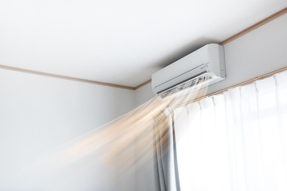 A white air conditioner is blowing air out of a window in a room — Gleeson's Air Conditioning in Wauchope, NSW