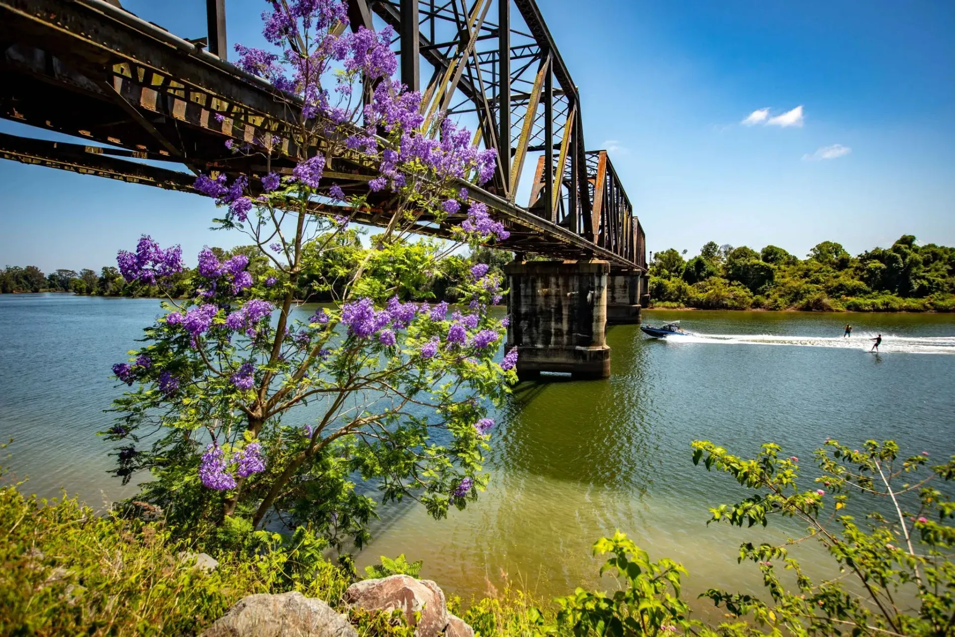 A Bridge with a Boat going Under it and Purple Flowers — Gleeson's Air Conditioning in Wauchope, NSW