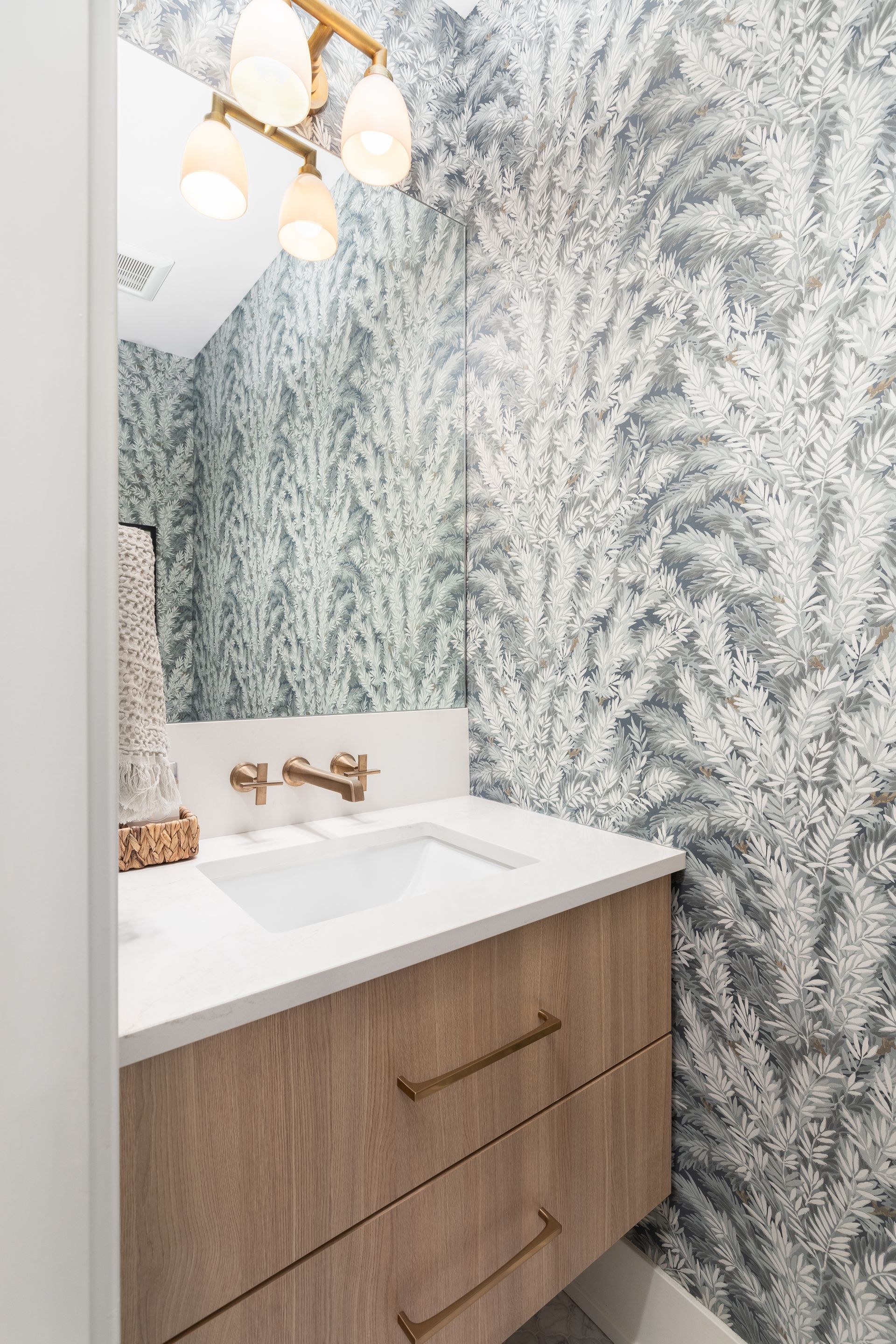 A bathroom with a sink , mirror , and wallpaper.