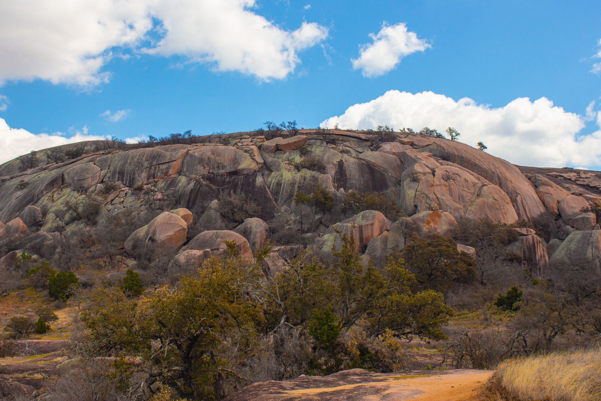 A large rocky hill with trees on it and a blue sky with clouds in the background.