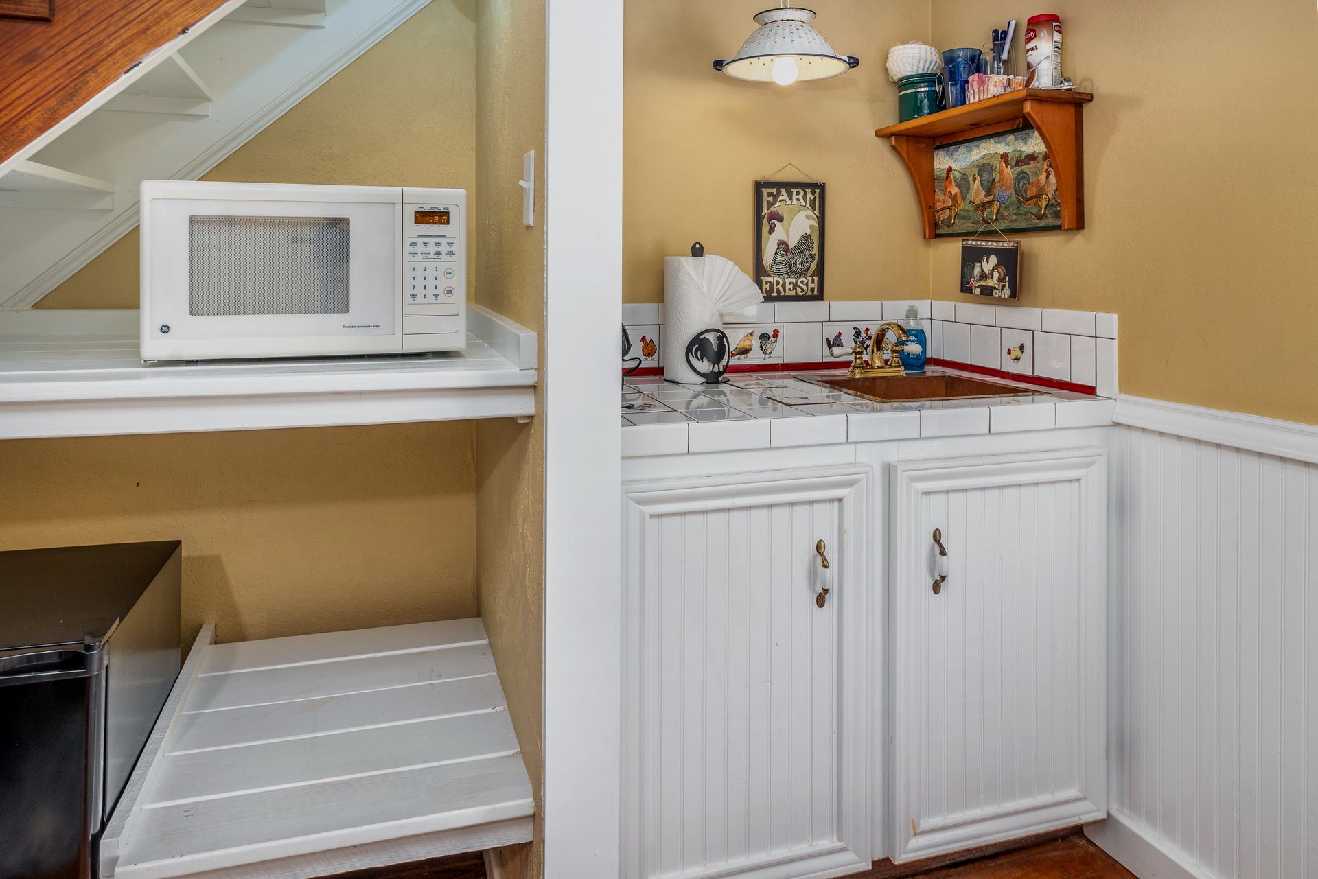 A kitchen with a microwave and a sink under stairs