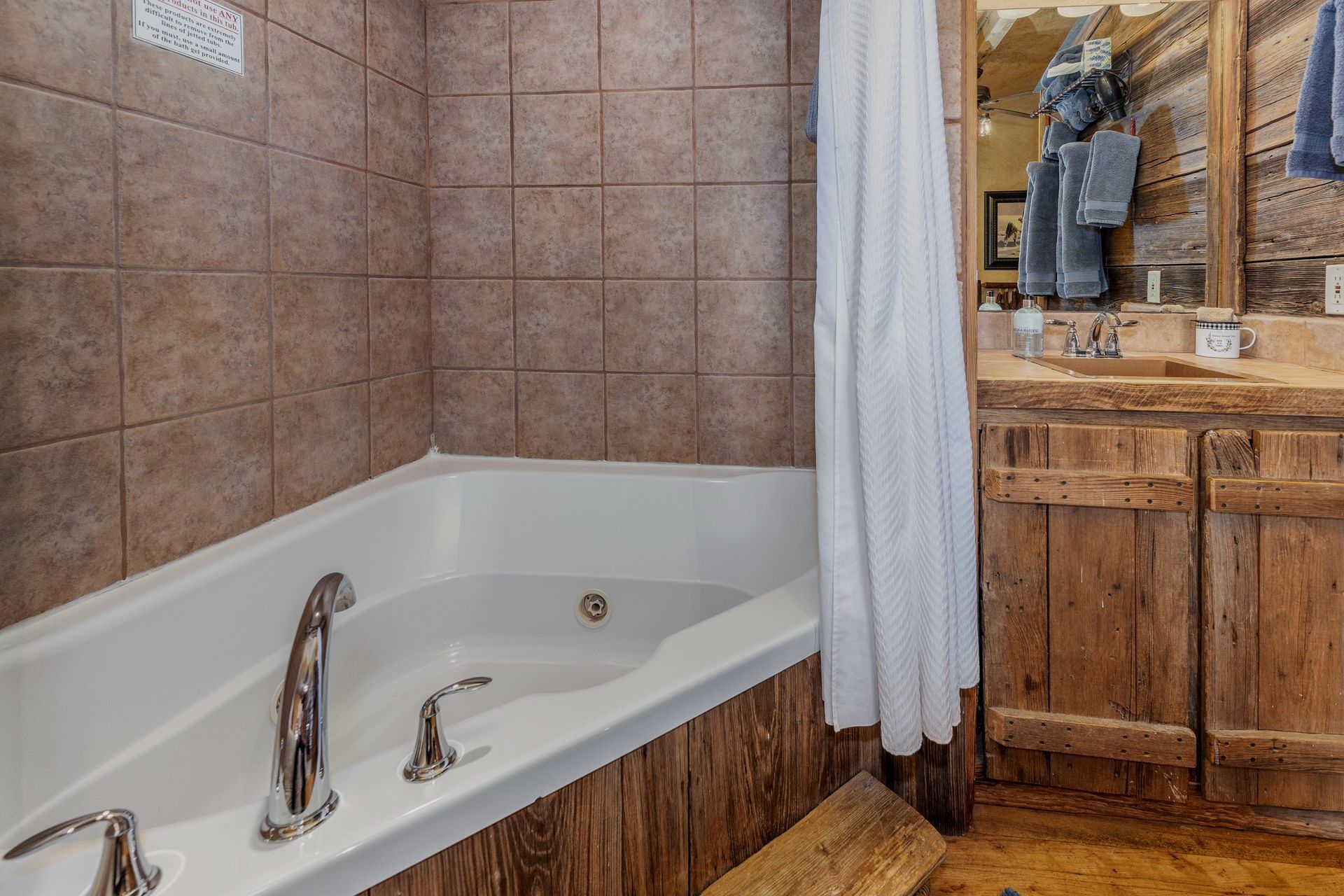 A bathroom with a tub , sink , mirror and wooden cabinets.