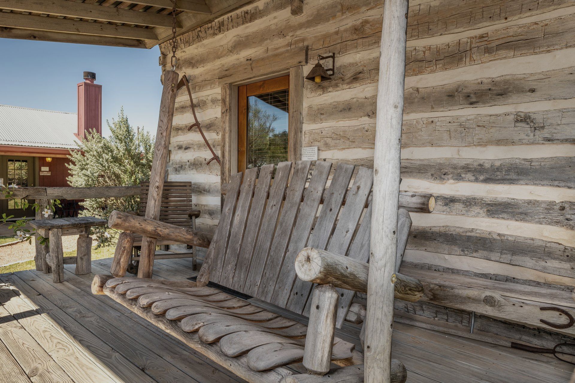 A wooden porch swing is on the porch of a log cabin.