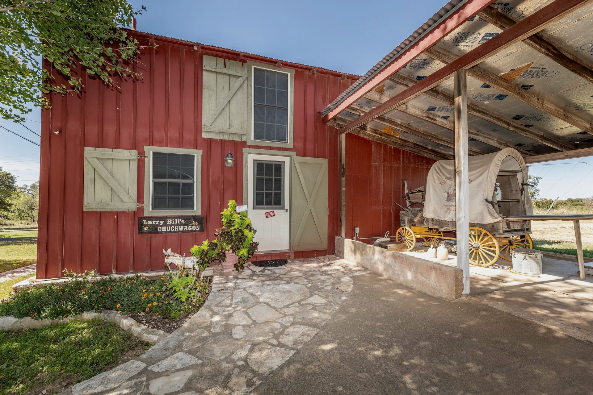 A red barn with a covered porch and a covered wagon in front of it.