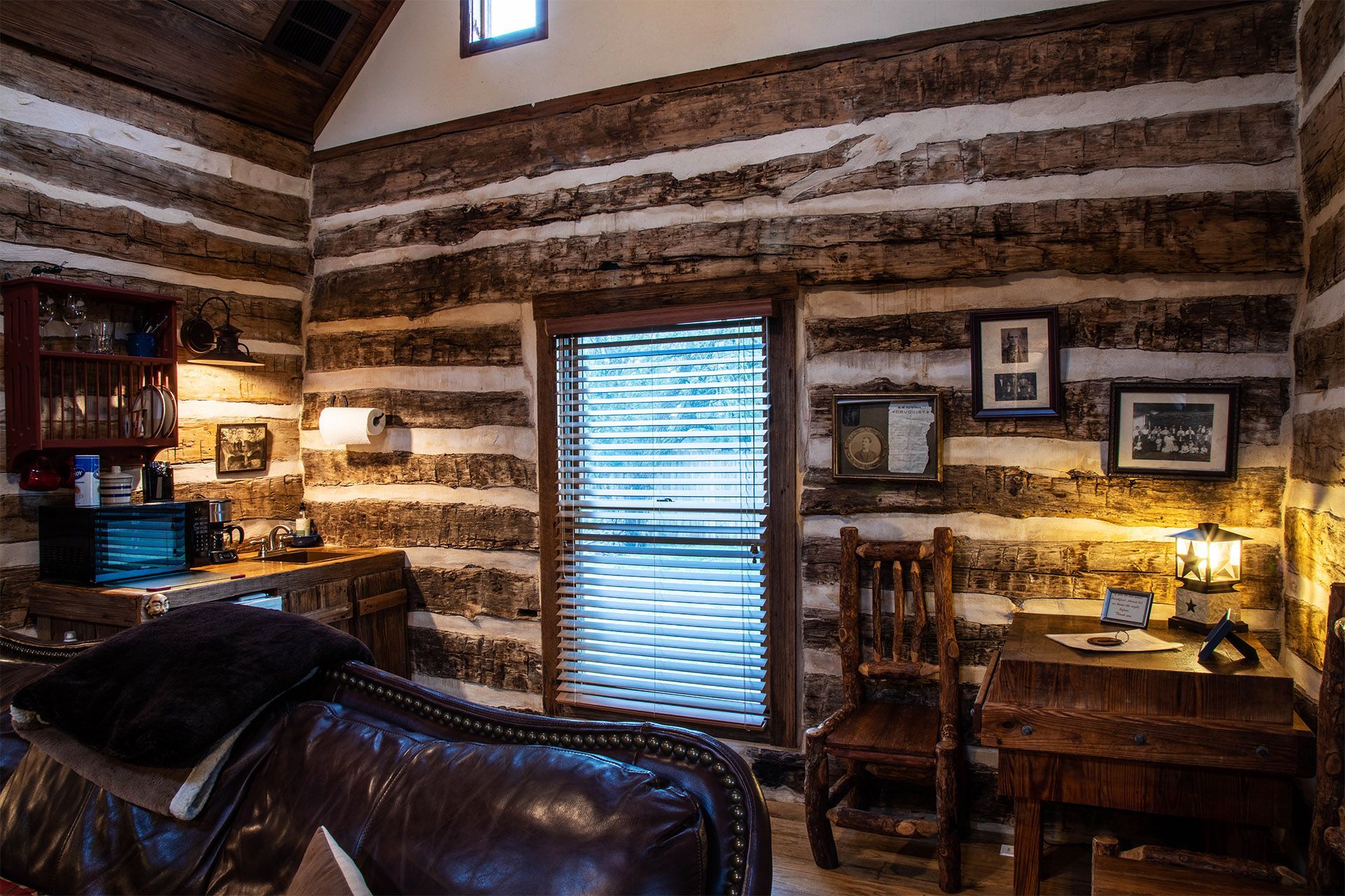 A living room in a log cabin with a couch , desk and chairs.