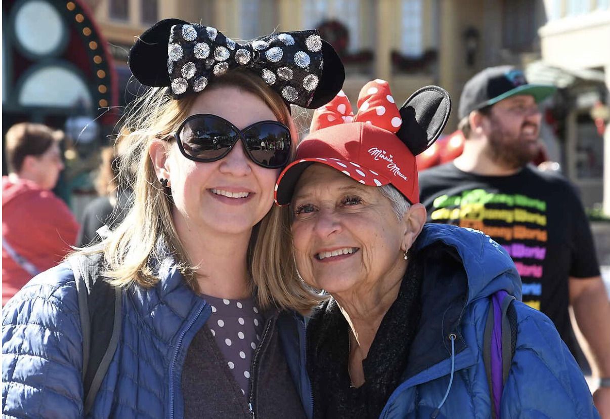 Two women wearing mickey mouse ears and hats are posing for a picture.