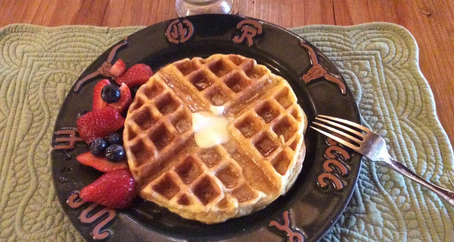 A waffle with butter and berries on a plate with a fork.