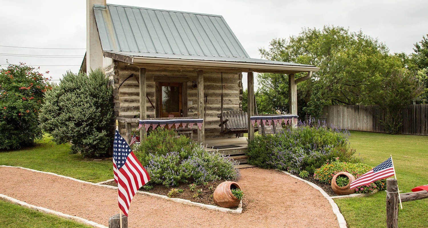 A small log cabin with an american flag in front of it.