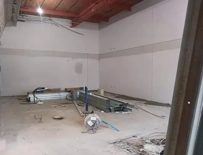 Interior of a room under construction, with exposed beams, drywall, and scattered building materials.