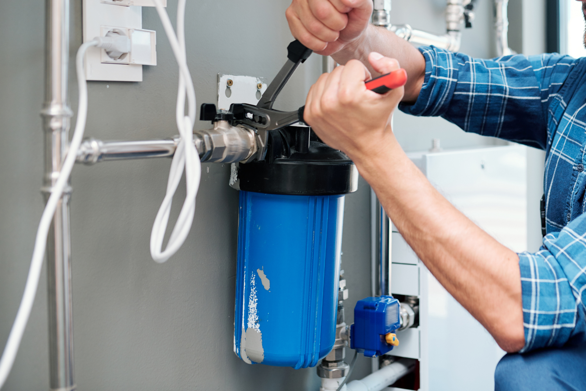 Plumber tightening a blue water filter housing under a sink with a wrench