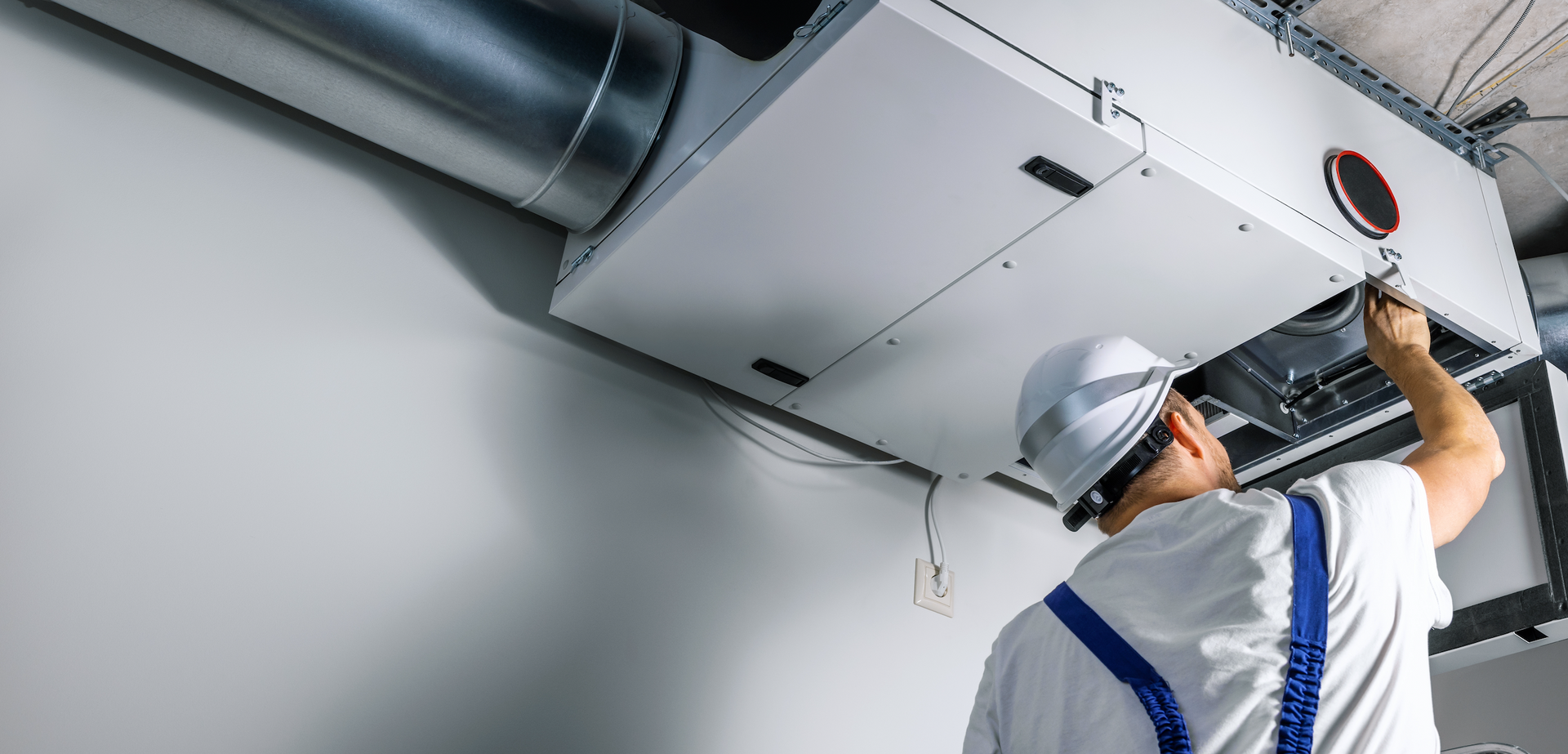 A man is working on a ventilation system in a building.