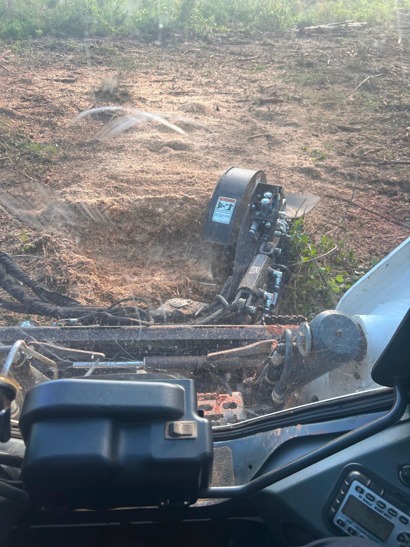 Skid steer with stump grinder removing a tree stump in a dirt area.