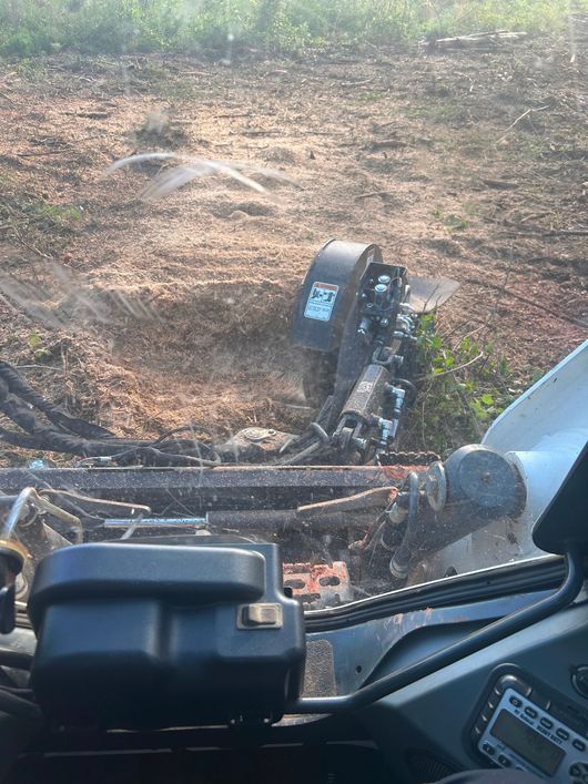 Skid steer with stump grinder removing a tree stump in a dirt area.