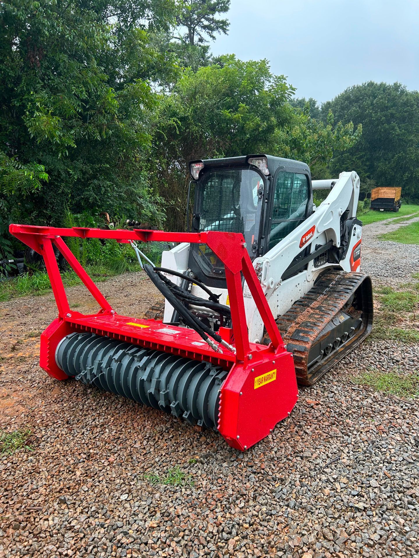 White and red Bobcat with a forestry mulcher attachment in a wooded area.