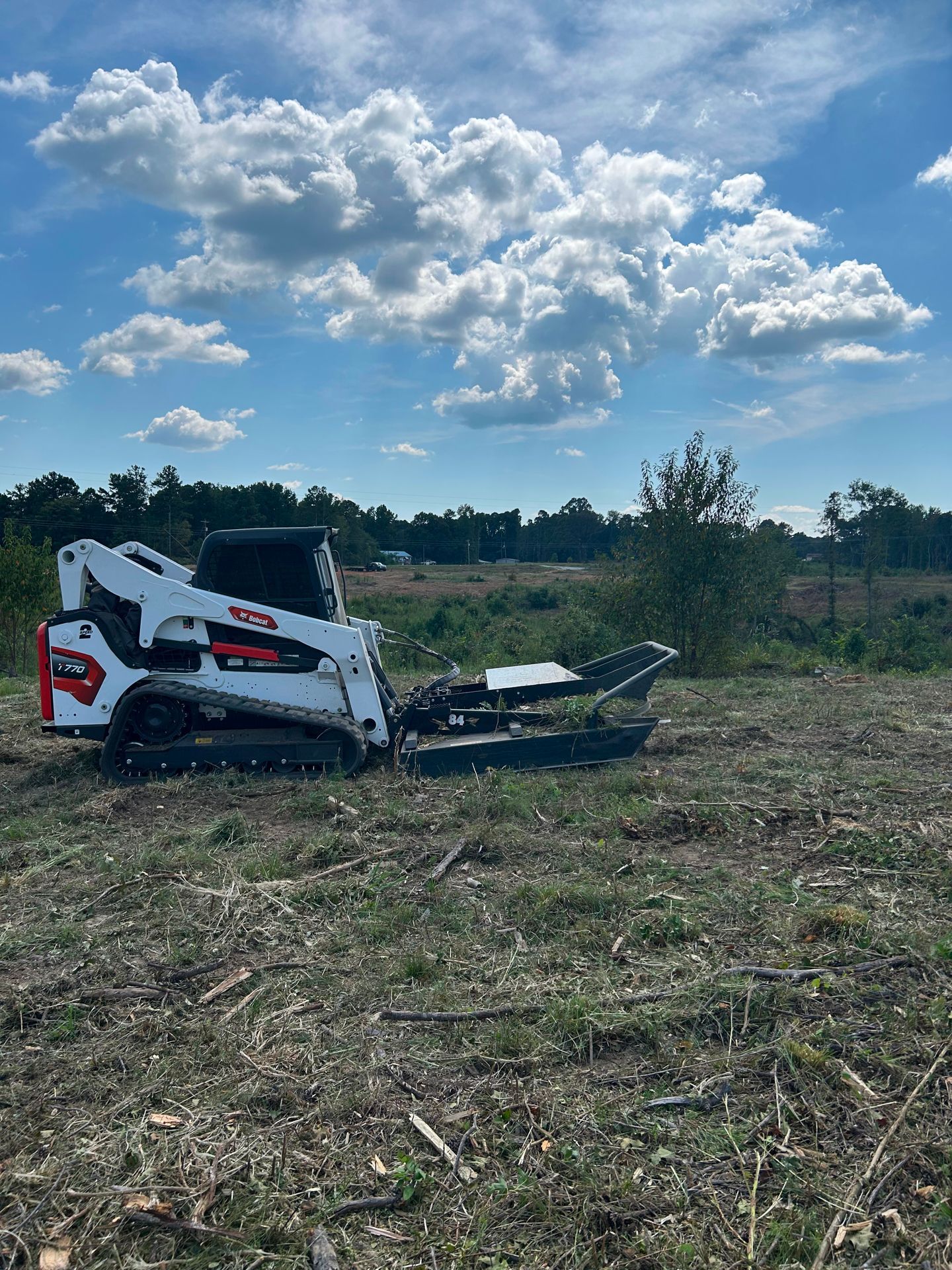 White Bobcat clearing land on a sunny day with scattered clouds.