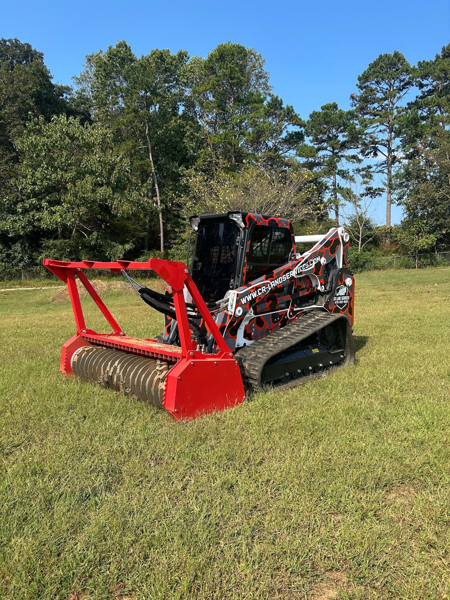 Red and black skid steer on tracks in a grassy field.