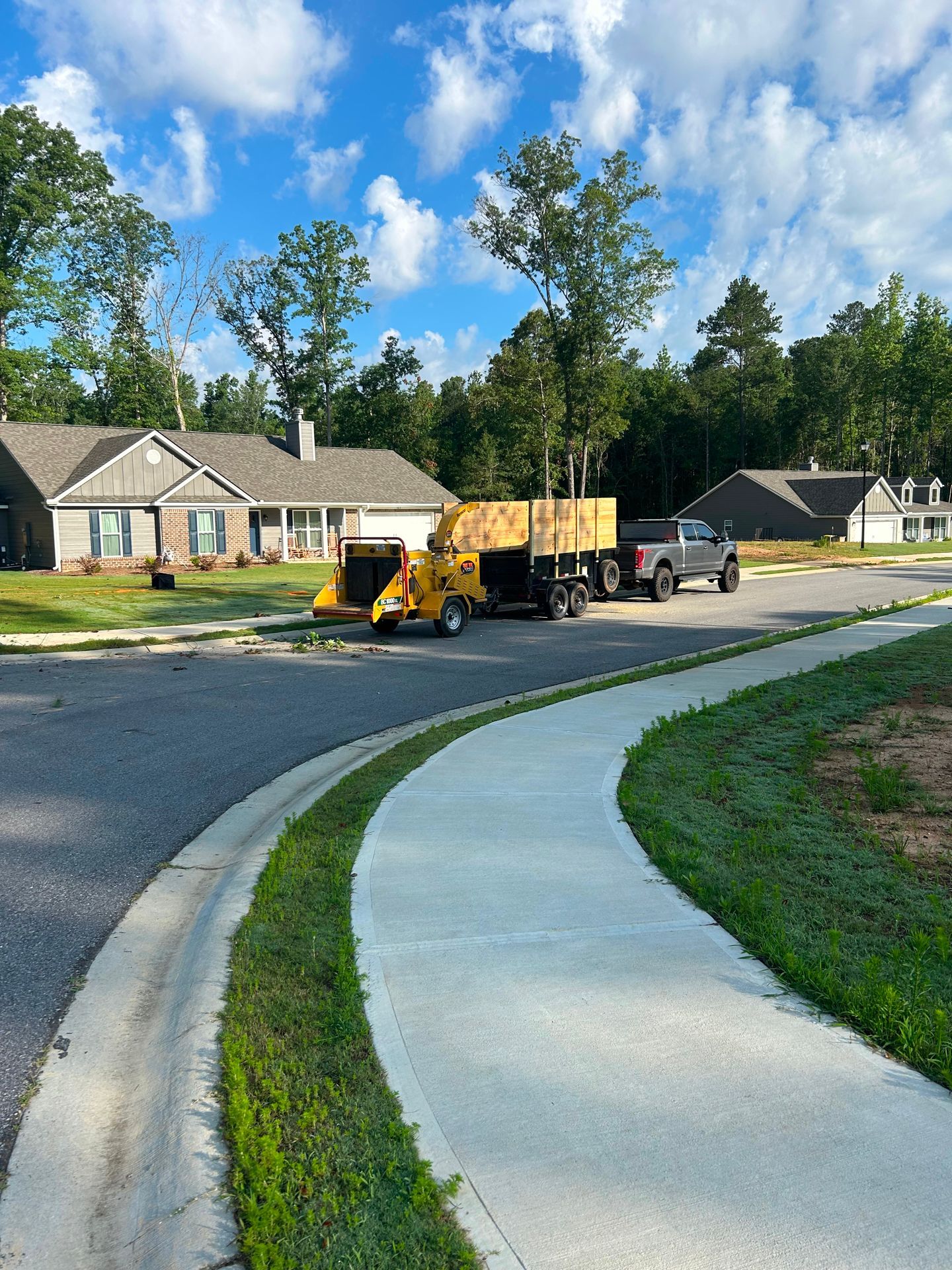 A wood chipper and truck hauling wood chips parked on a residential street.