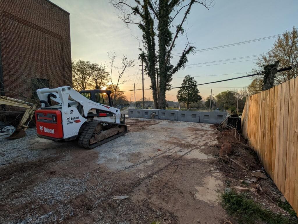 Bobcat skid-steer loader on gravel surface next to a wooden fence and gray barriers at dusk.