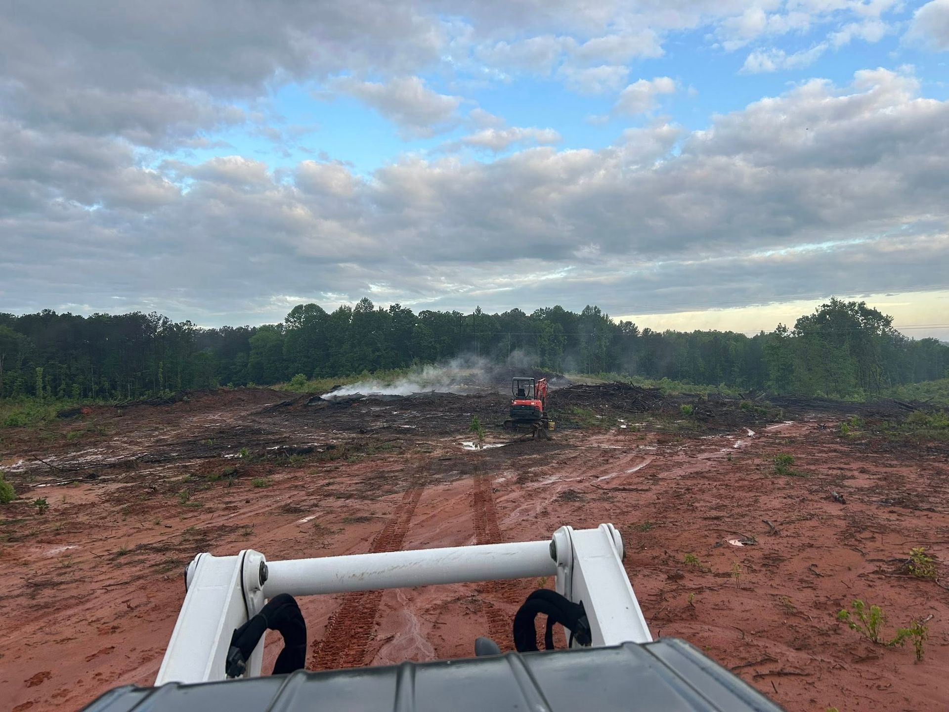 Muddy field with construction equipment; forest in background, overcast sky.