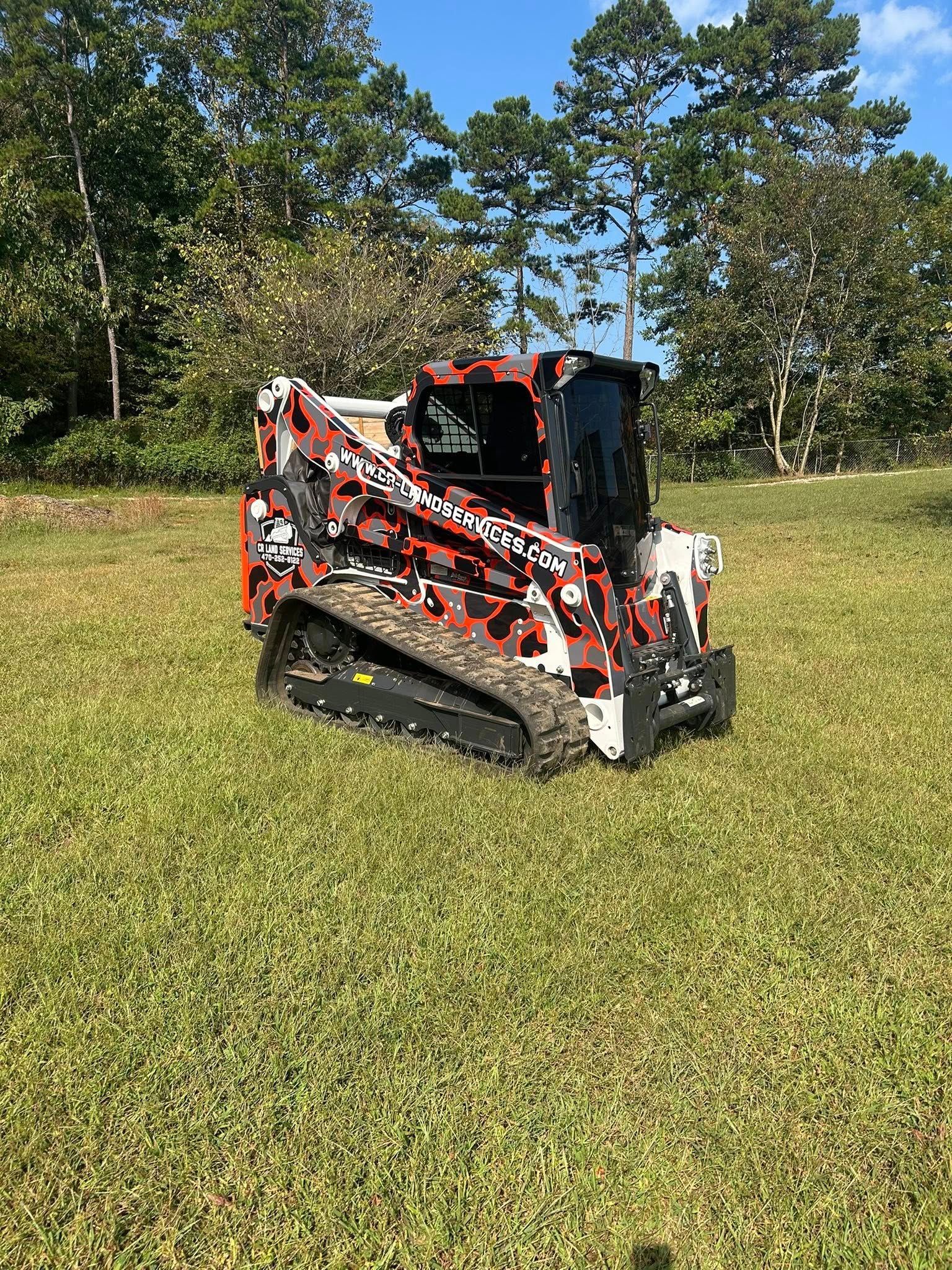 Tracked skid steer with orange and white camouflage design on grassy field.