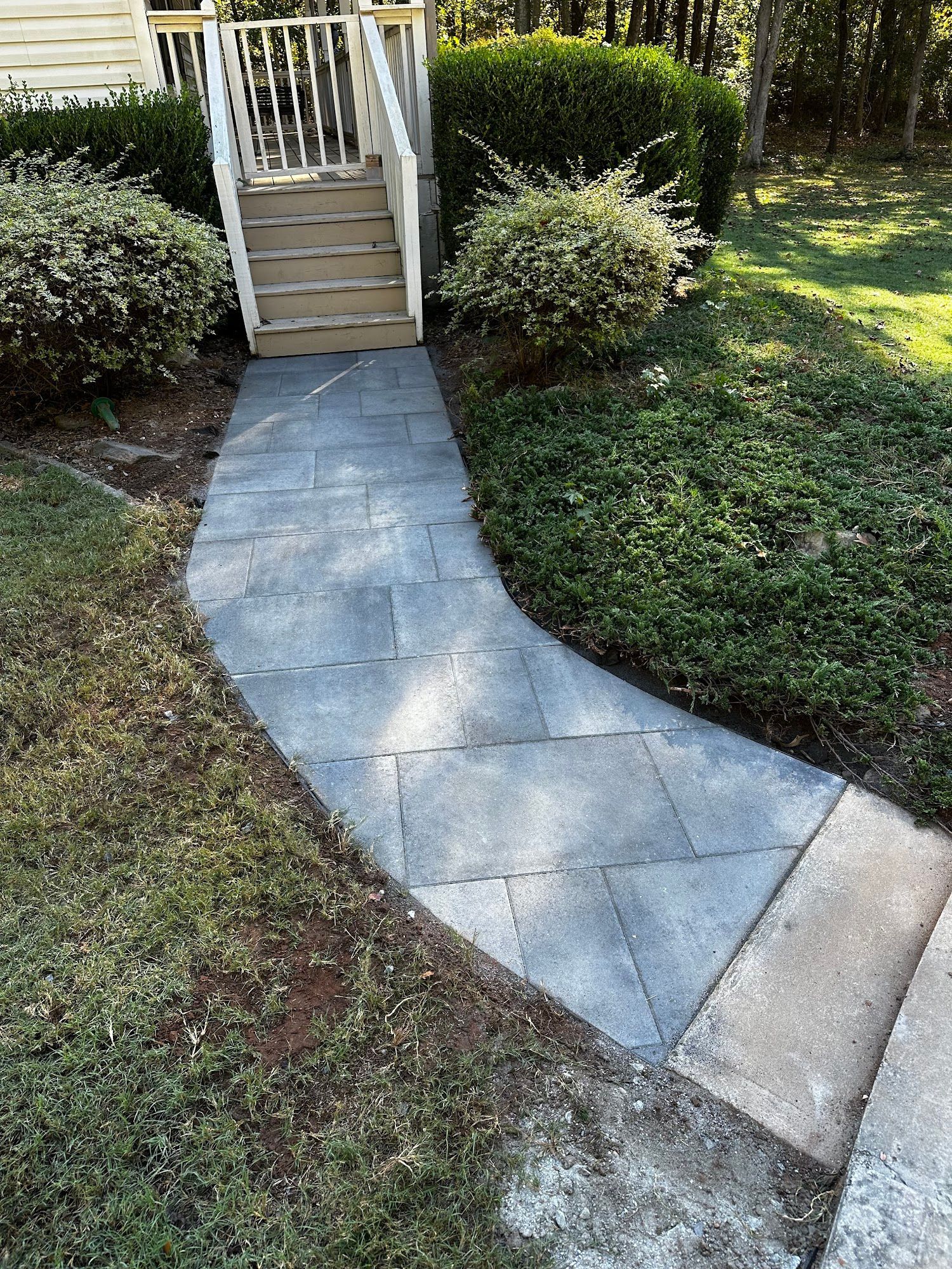 Stone pathway curving towards a deck, flanked by greenery and steps.