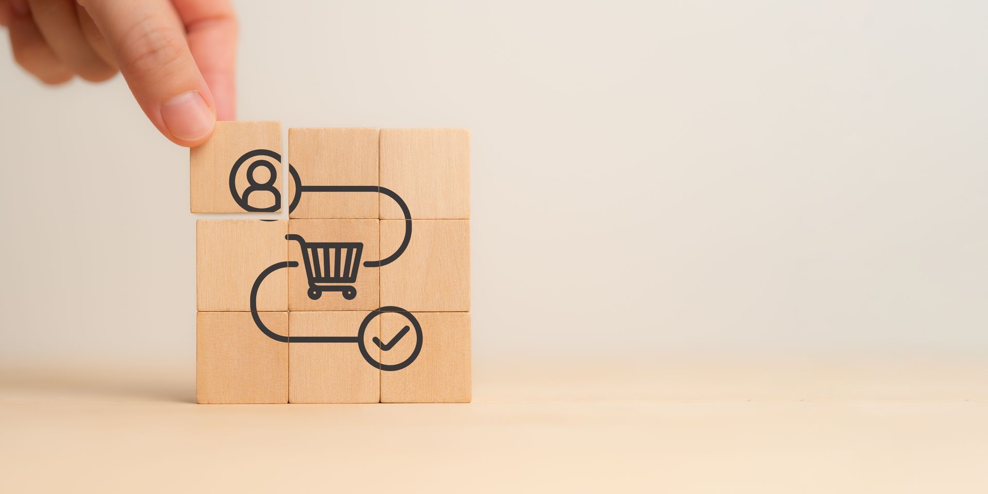 A person is holding a wooden block with a shopping cart icon on it.