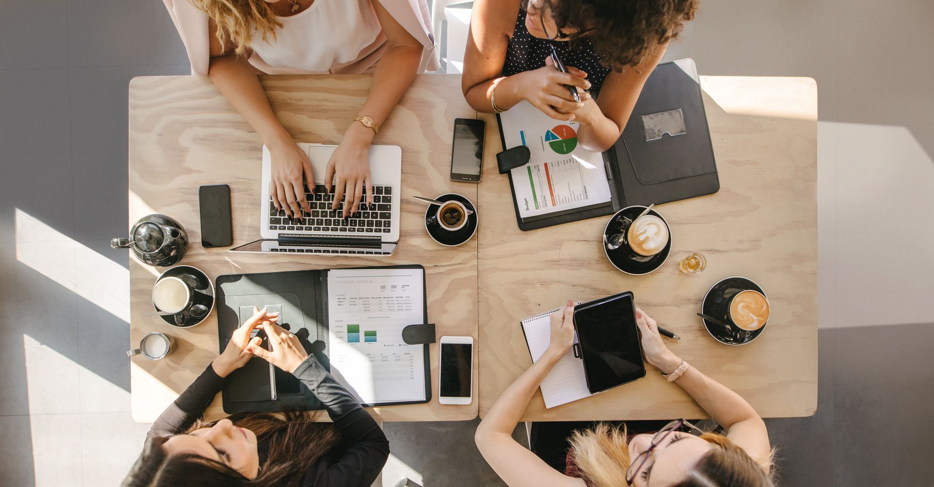A group of women are sitting at a table with laptops and tablets.