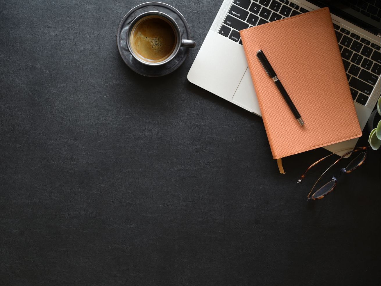 A cup of coffee , a notebook , a pen , and a laptop on a desk.